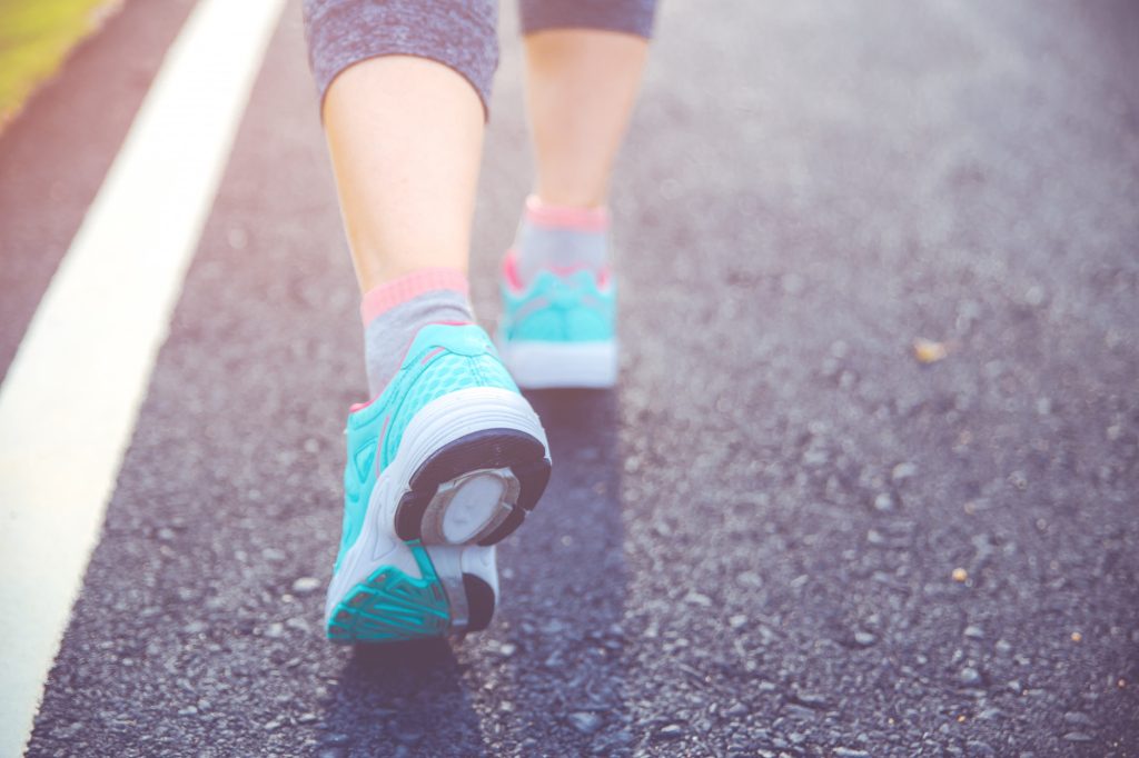 Ciérrese para arriba en el zapato, pies de atleta del corredor que corren en el camino bajo luz del sol en la mañana.