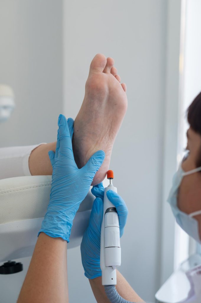 El podólogo trata los pies usando una máquina de dispositivos eléctricos Paciente en un procedimiento de pedicura médica