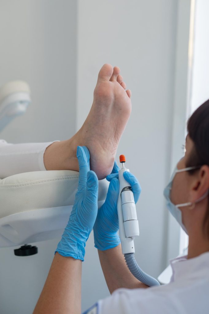 El podólogo trata los pies usando una máquina de dispositivos eléctricos Paciente en un procedimiento de pedicura médica