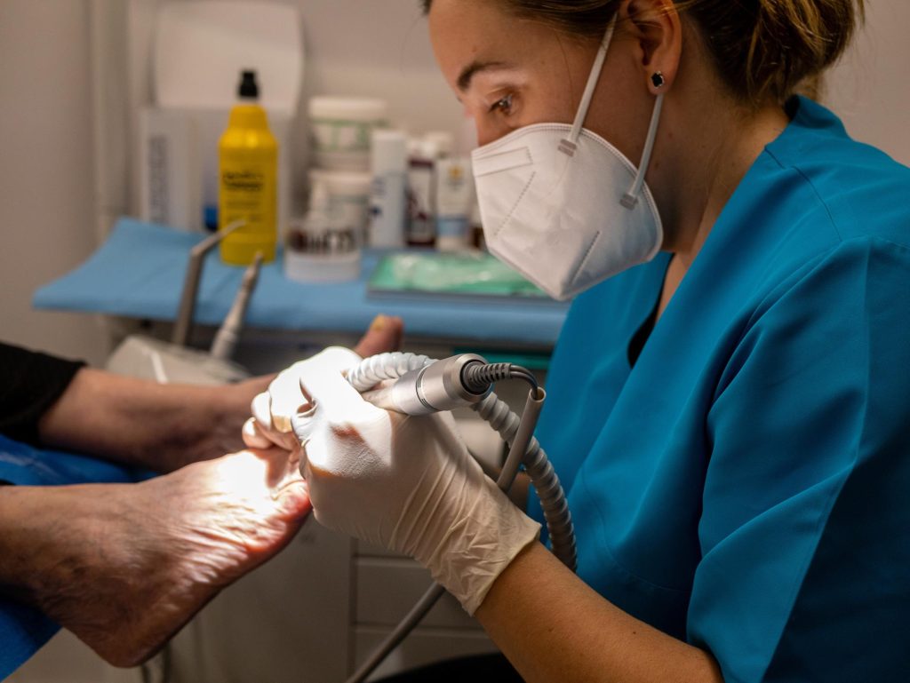 Podóloga con mascarilla médica y guantes que tratan los pies de un cliente